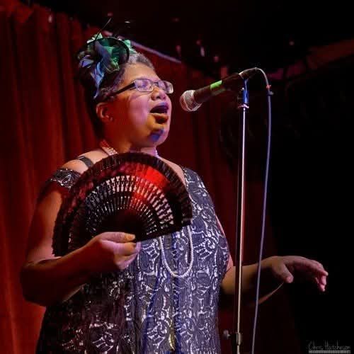 At nerd girl burlesque singing Miss Celie's Blues wearing lace dress, green fascinator and holding black fan